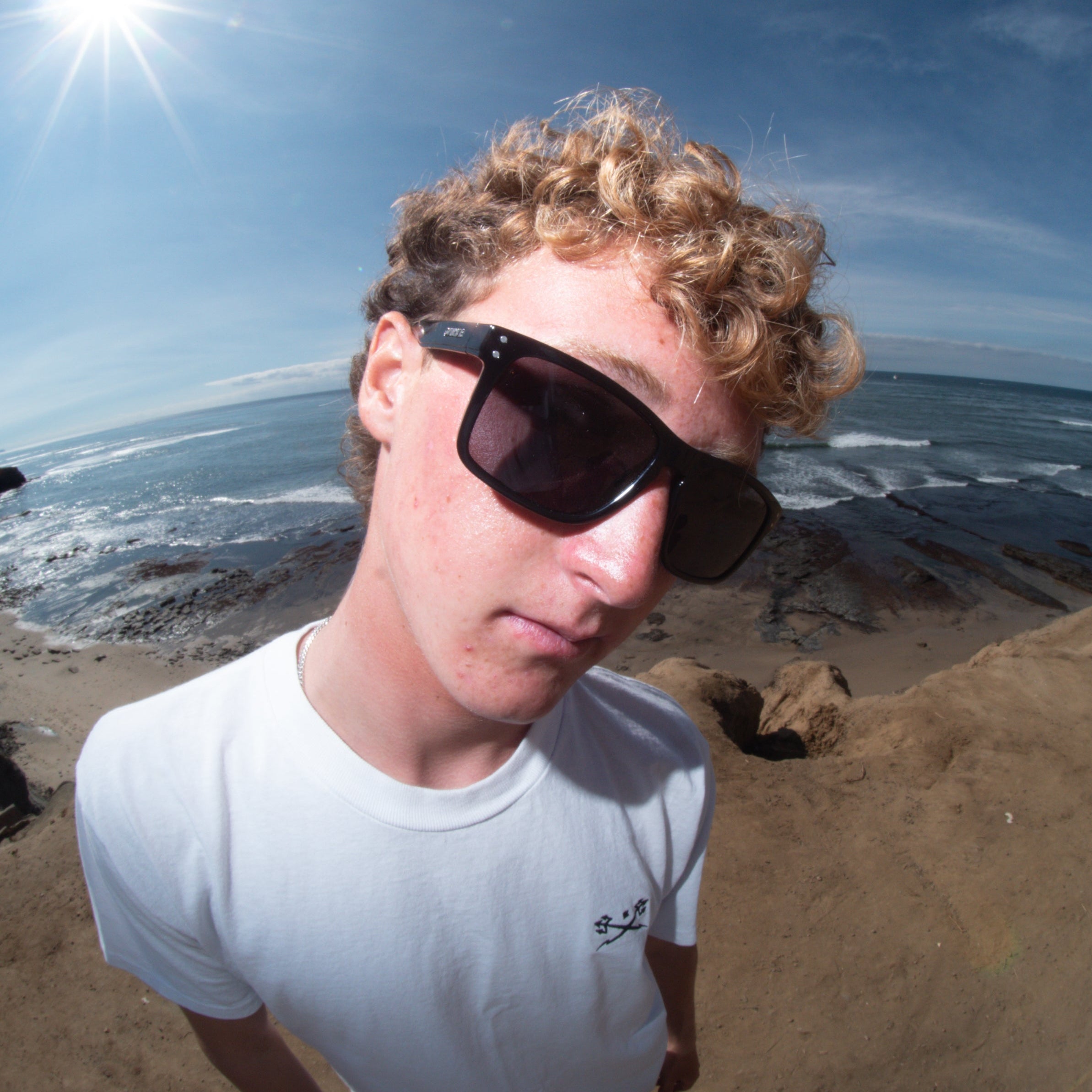 Person wearing sunglasses on a beach with ocean and sky in the background