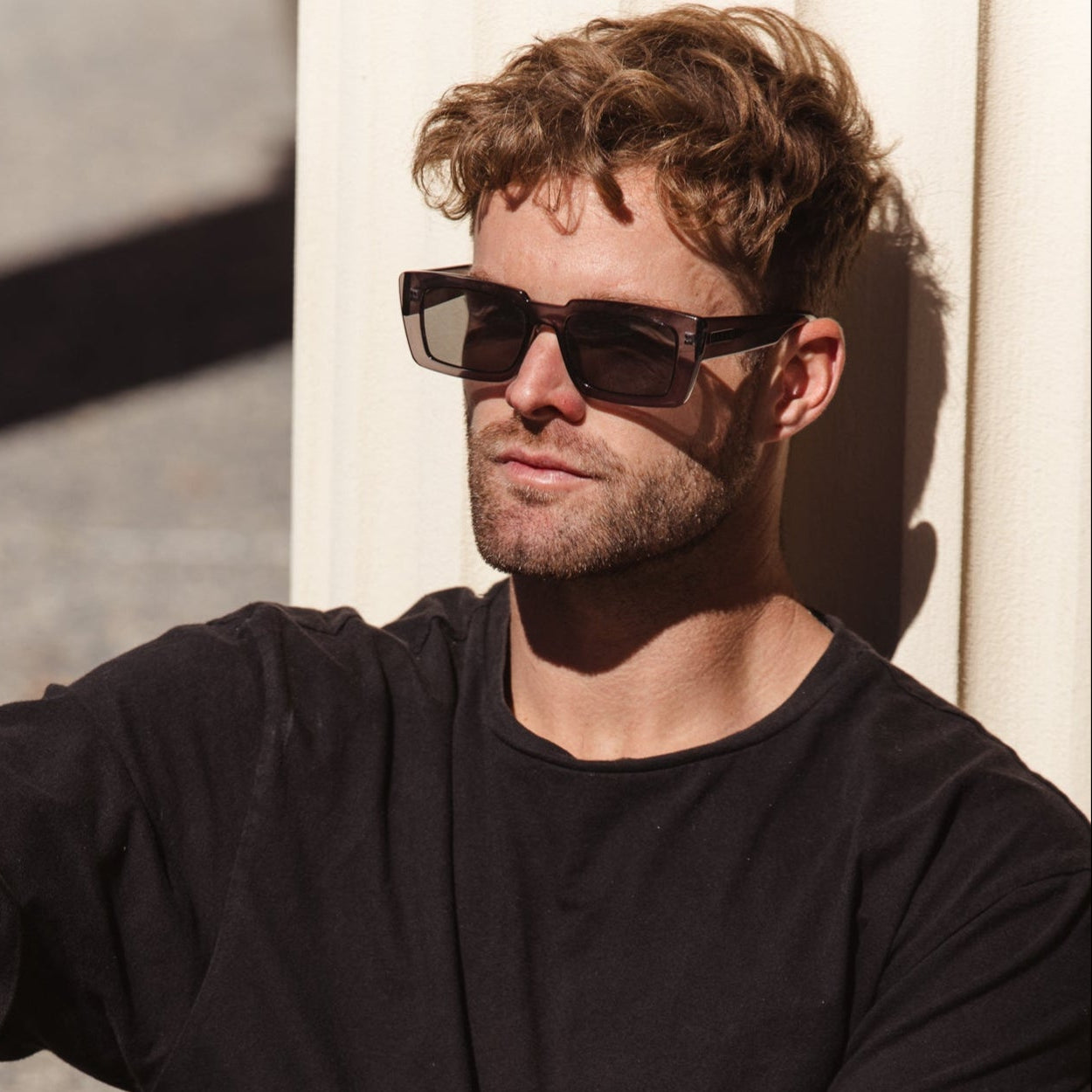 Man wearing sunglasses and a black shirt against a neutral background
