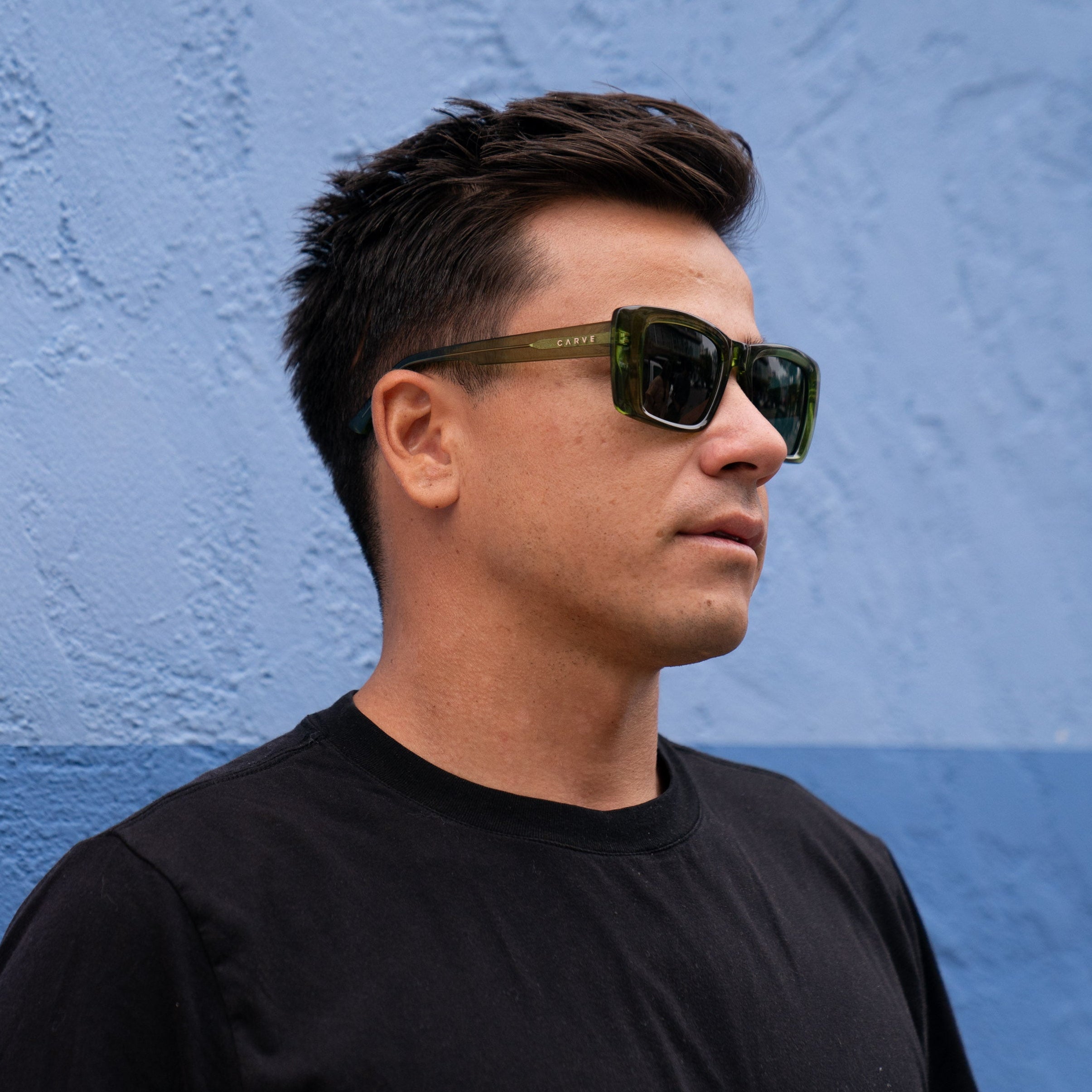 Man wearing sunglasses and a black shirt against a blue wall