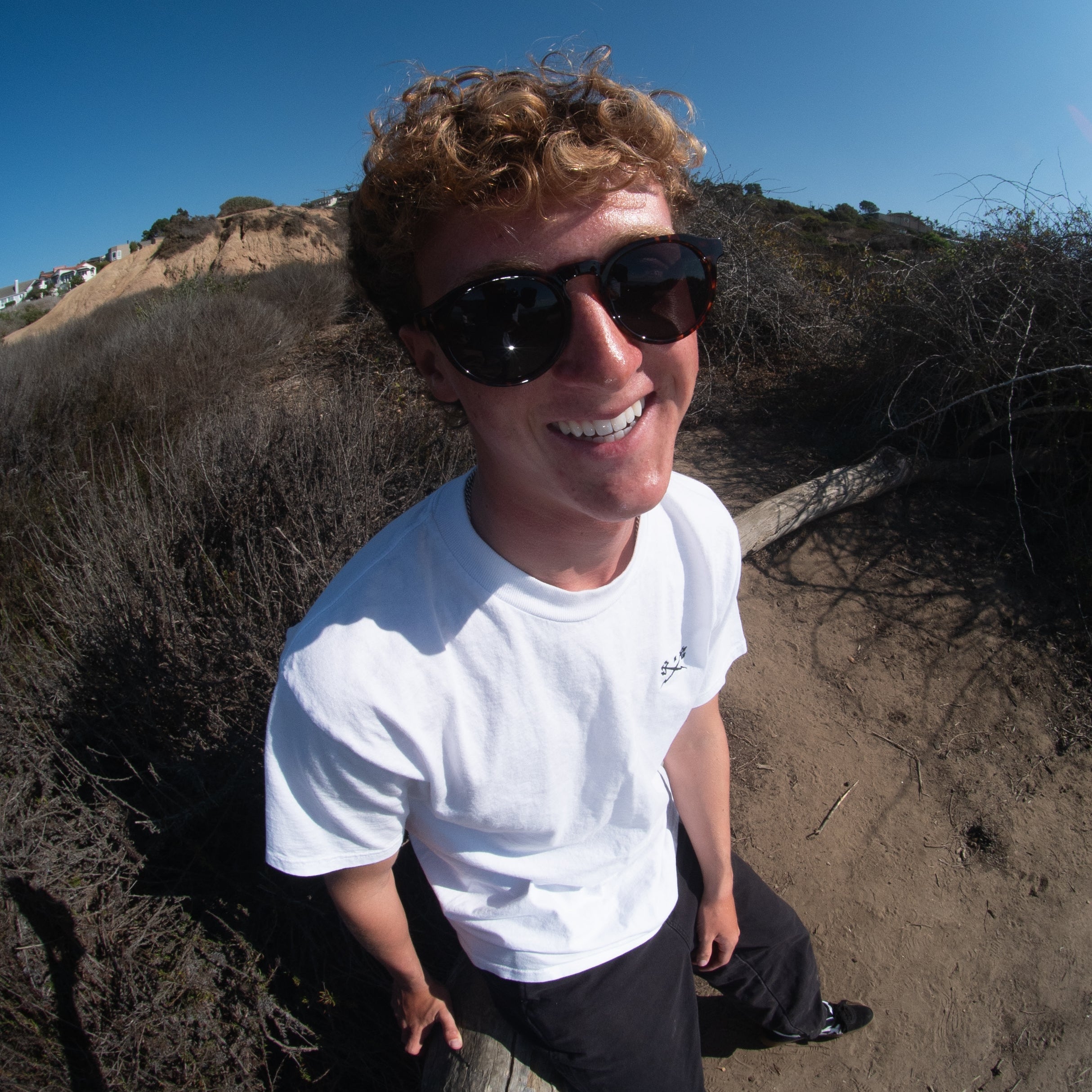 Person wearing sunglasses and a white shirt on a beach