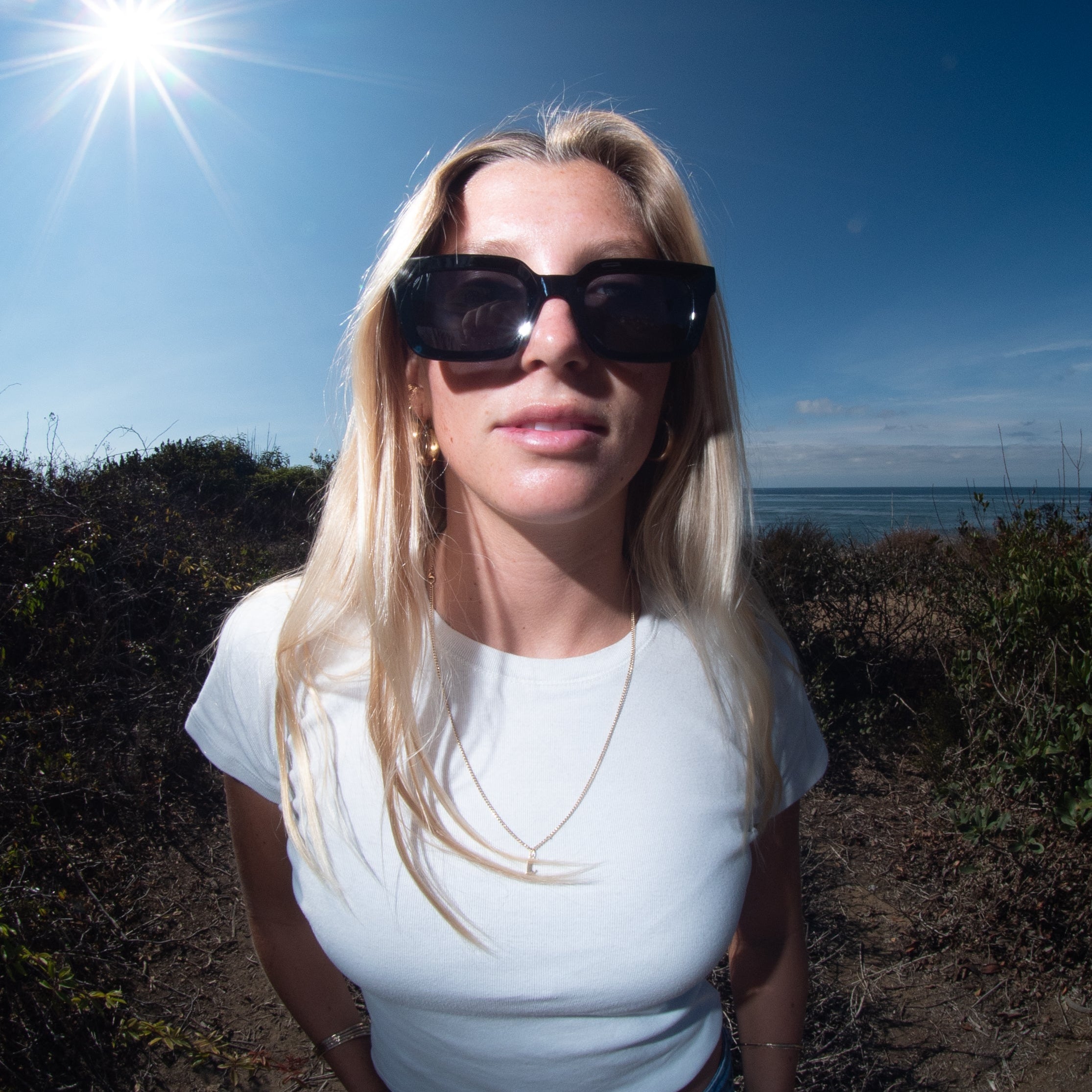 Woman wearing sunglasses and a white shirt with a blue background