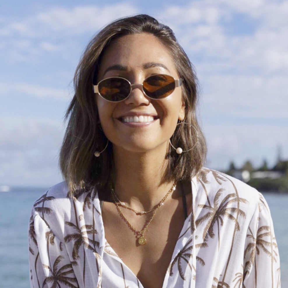 Woman wearing sunglasses and a patterned shirt with a beach background