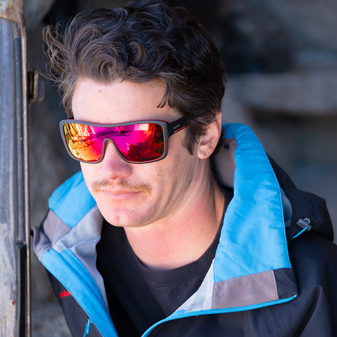 Man wearing reflective sunglasses and a blue jacket with a blurred background