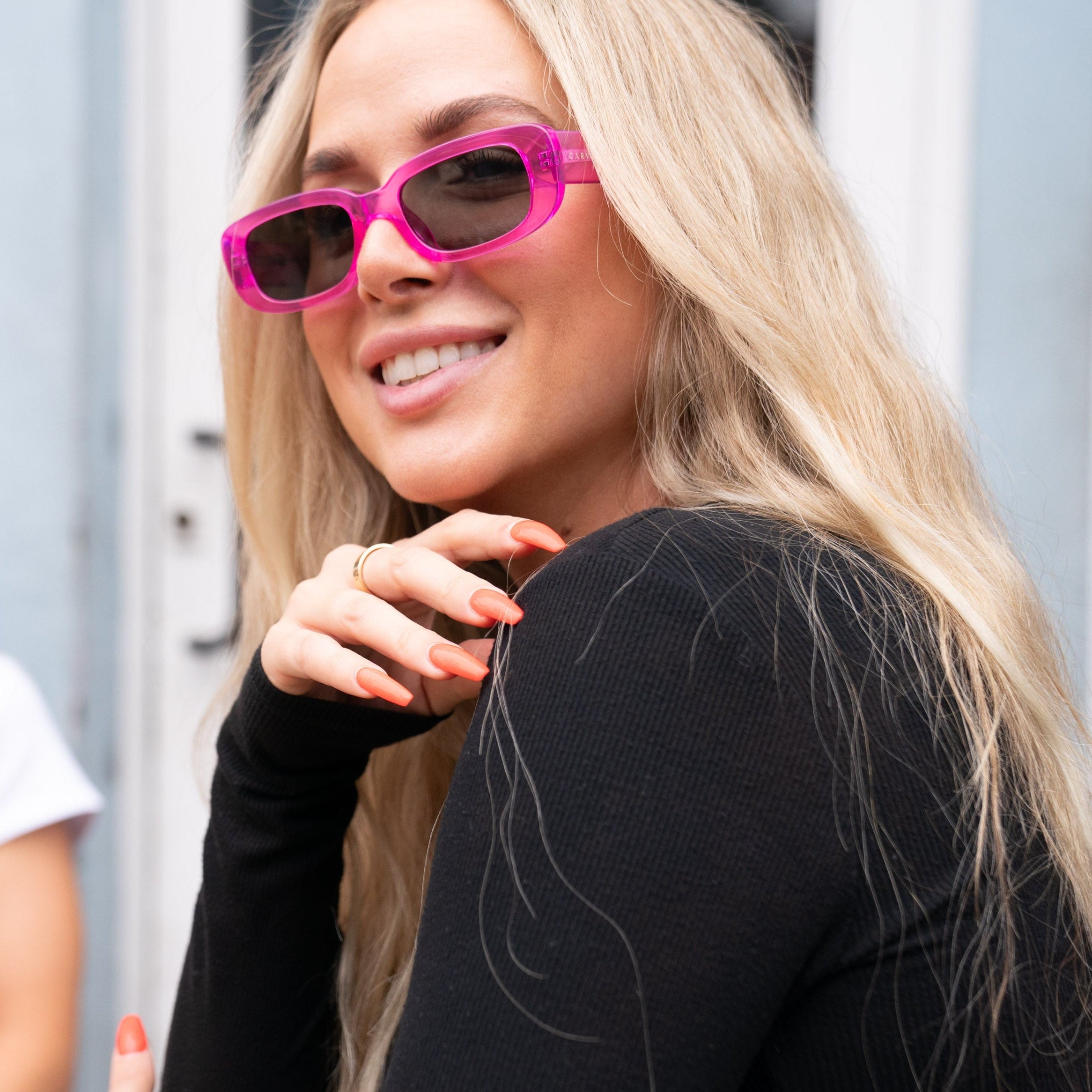Two women wearing sunglasses outdoors, one with pink sunglasses and a black top.