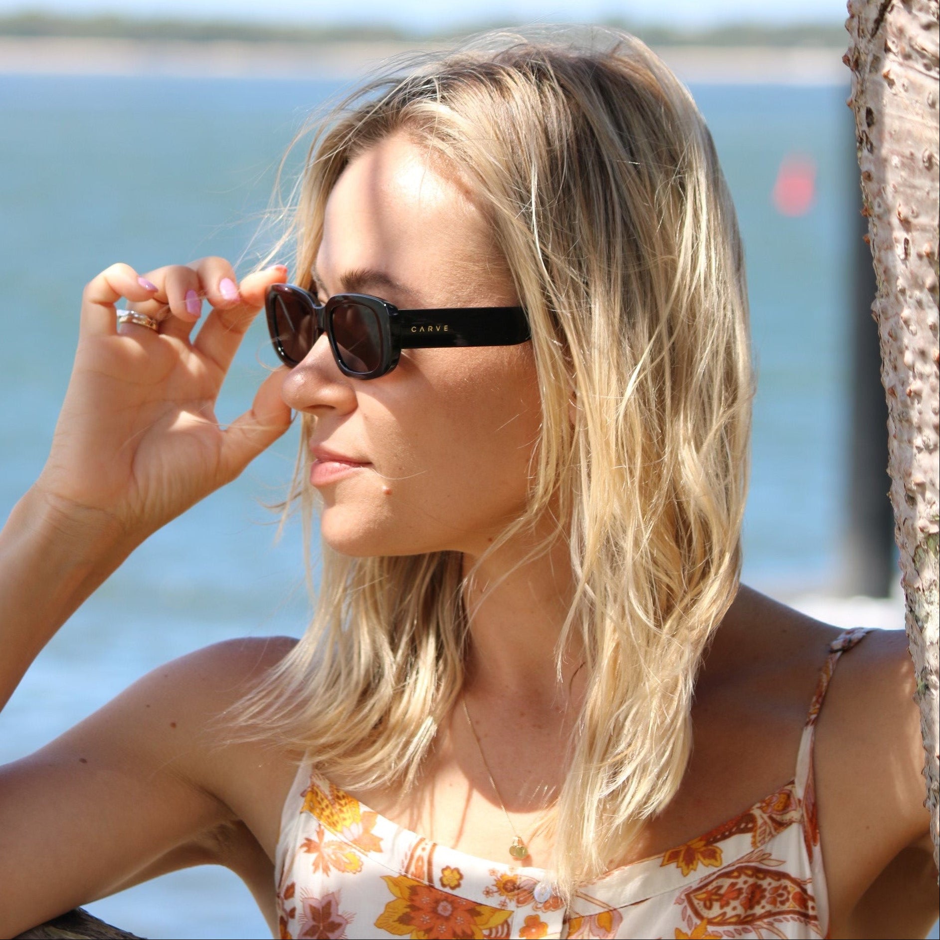 Woman with sunglasses on a sunny day, leaning against a tree