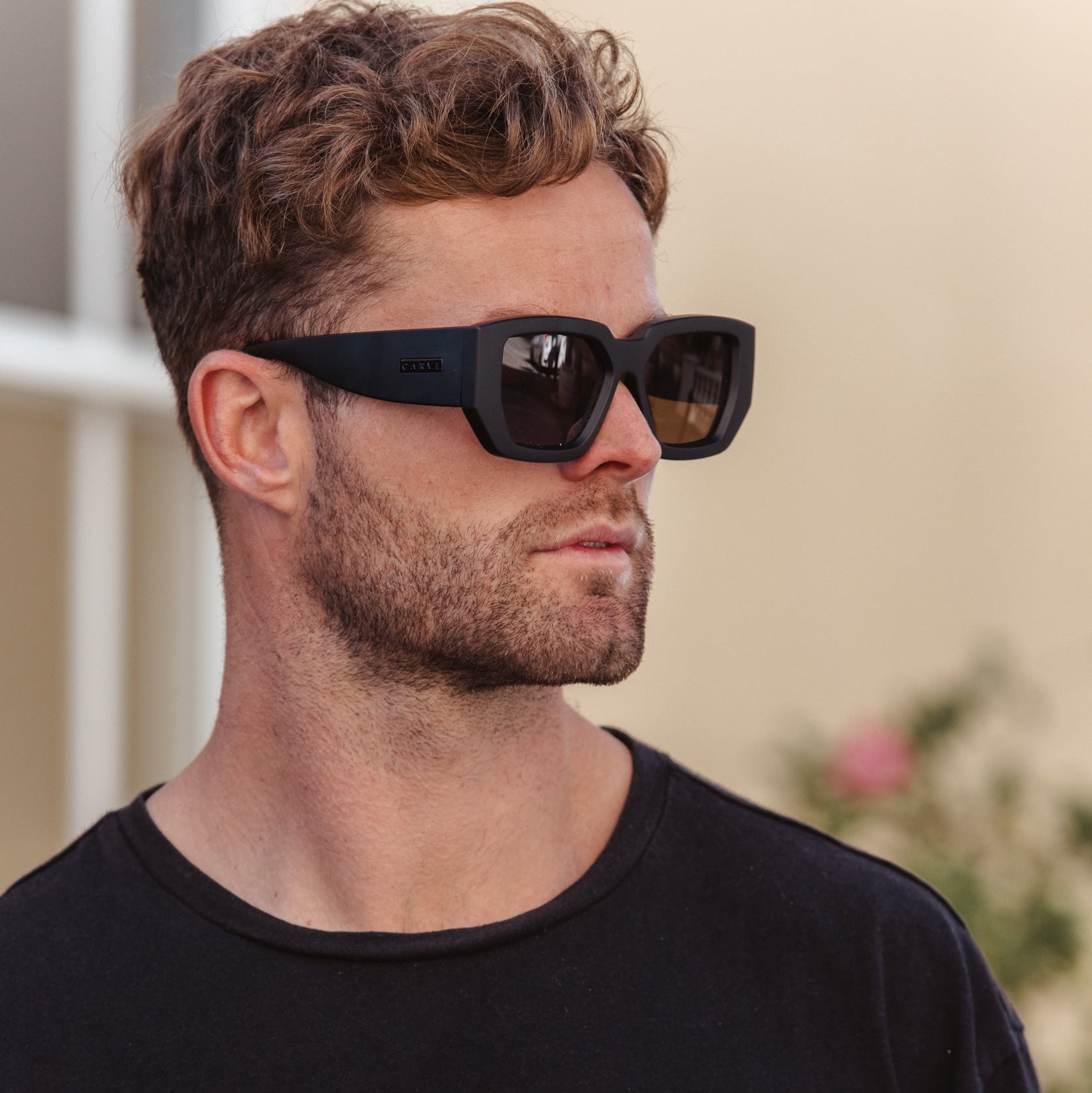 Man wearing black sunglasses and a black shirt with a blurred background