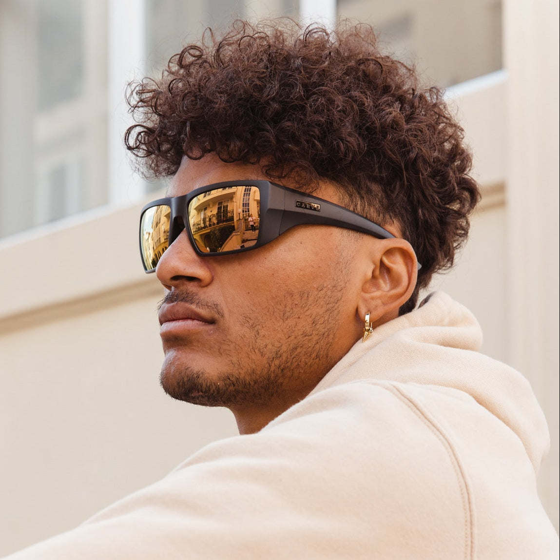 Man wearing sunglasses and a beige hoodie sitting outdoors.