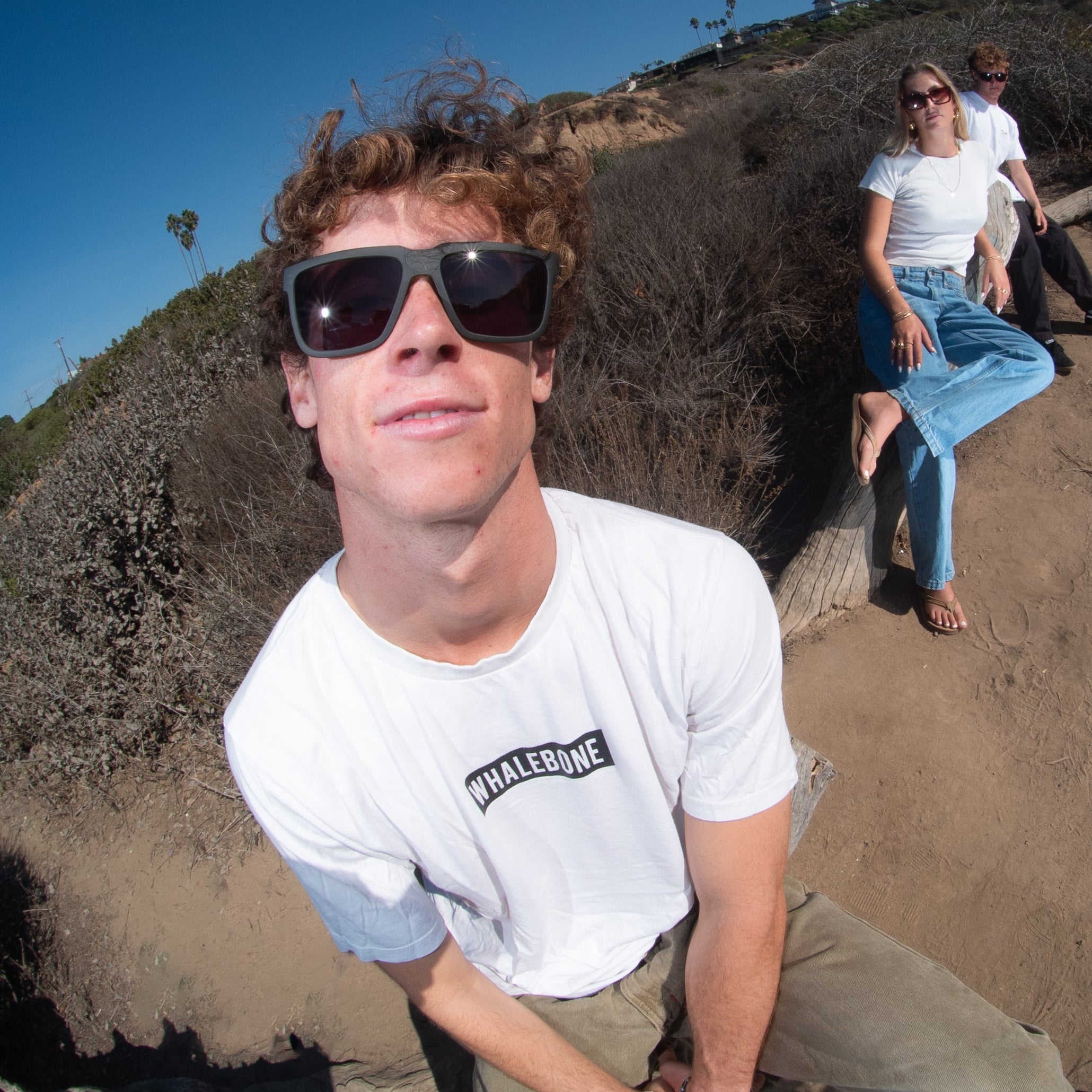 Fisheye lens view of two people on a dirt path with a clear blue sky.