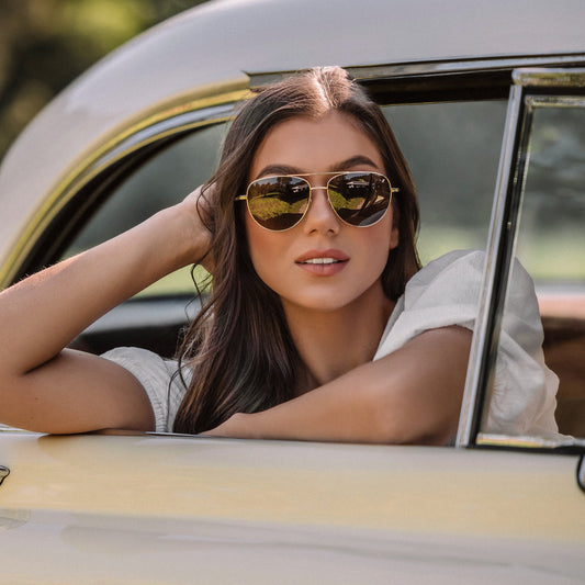 Woman wearing sunglasses sitting in a vintage car with trees in the background
