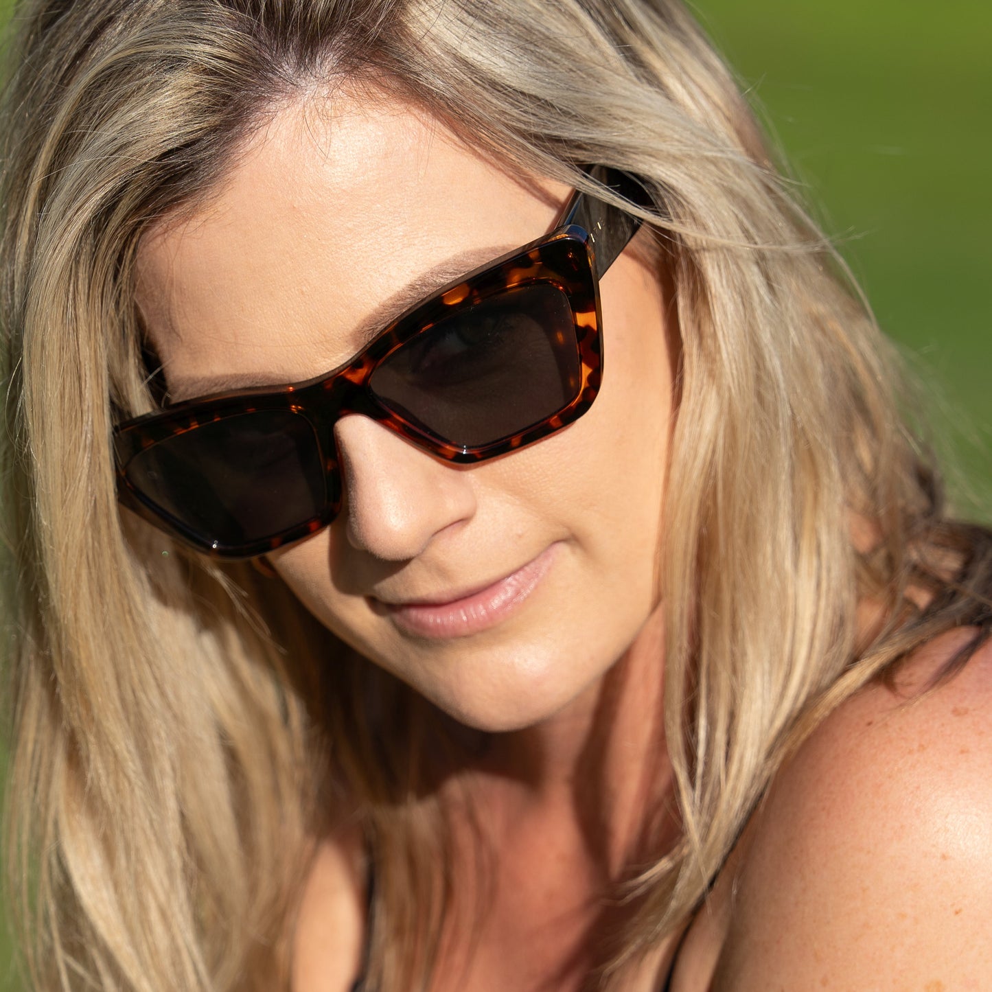 Woman wearing tortoiseshell sunglasses with a blurred green background