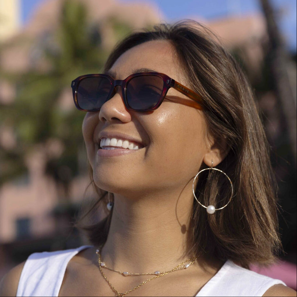 Woman wearing sunglasses and hoop earrings with a blurred outdoor background