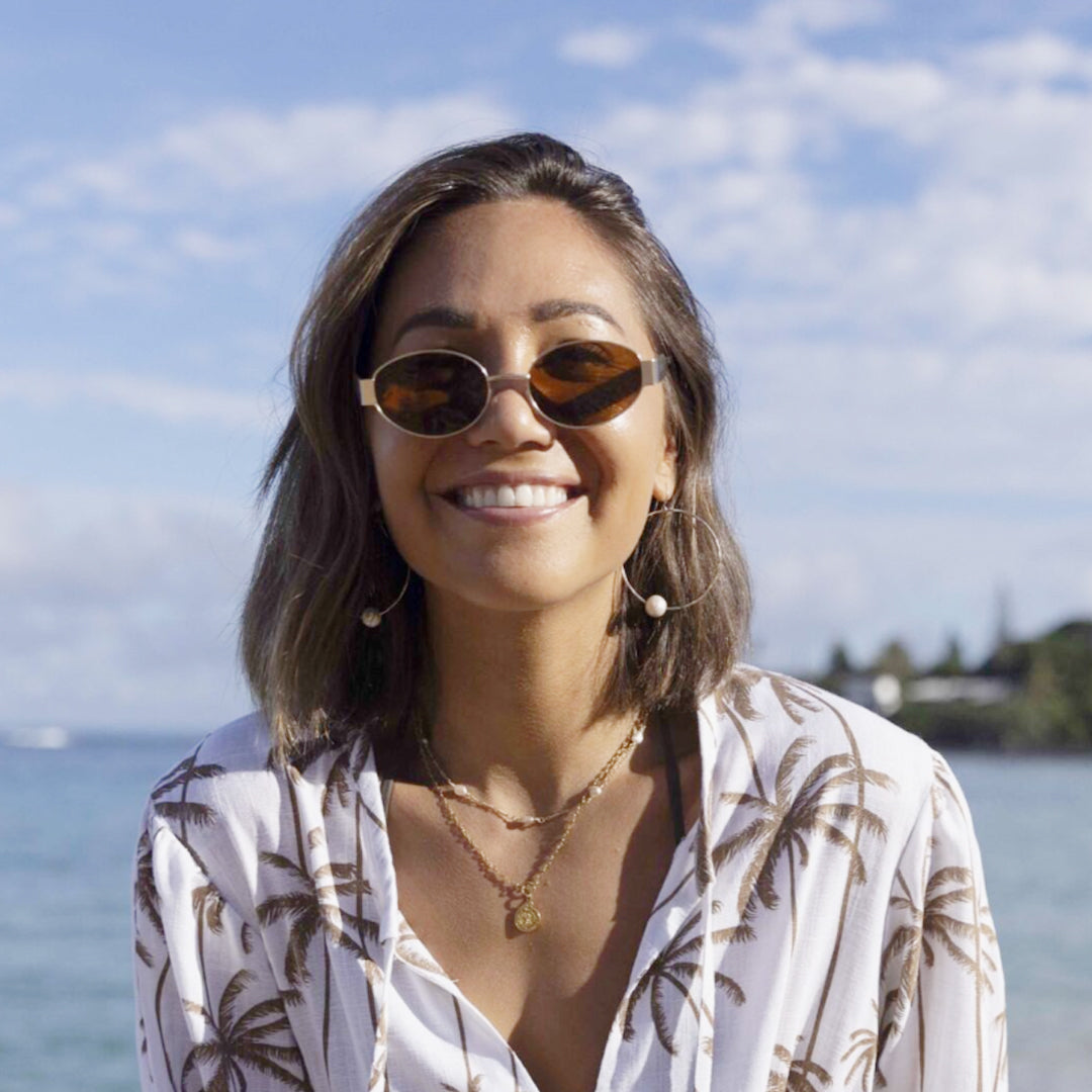 Woman wearing sunglasses and a patterned shirt with a beach background