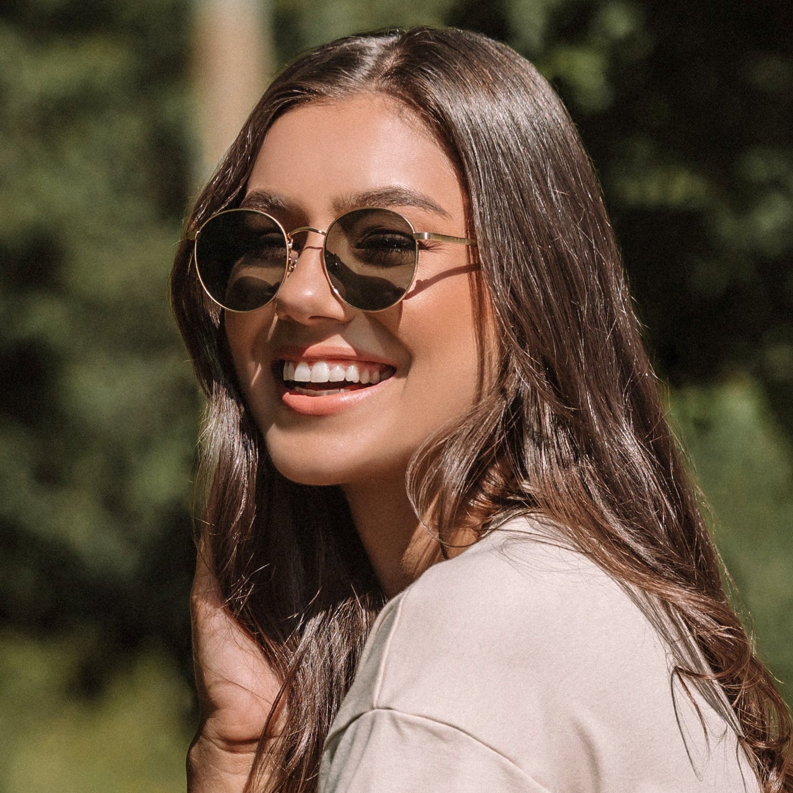Woman in denim shorts and sunglasses leaning against a white picket fence with a vintage car in the background.