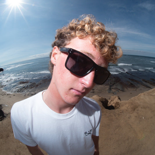 Person wearing sunglasses on a beach with ocean and sky in the background