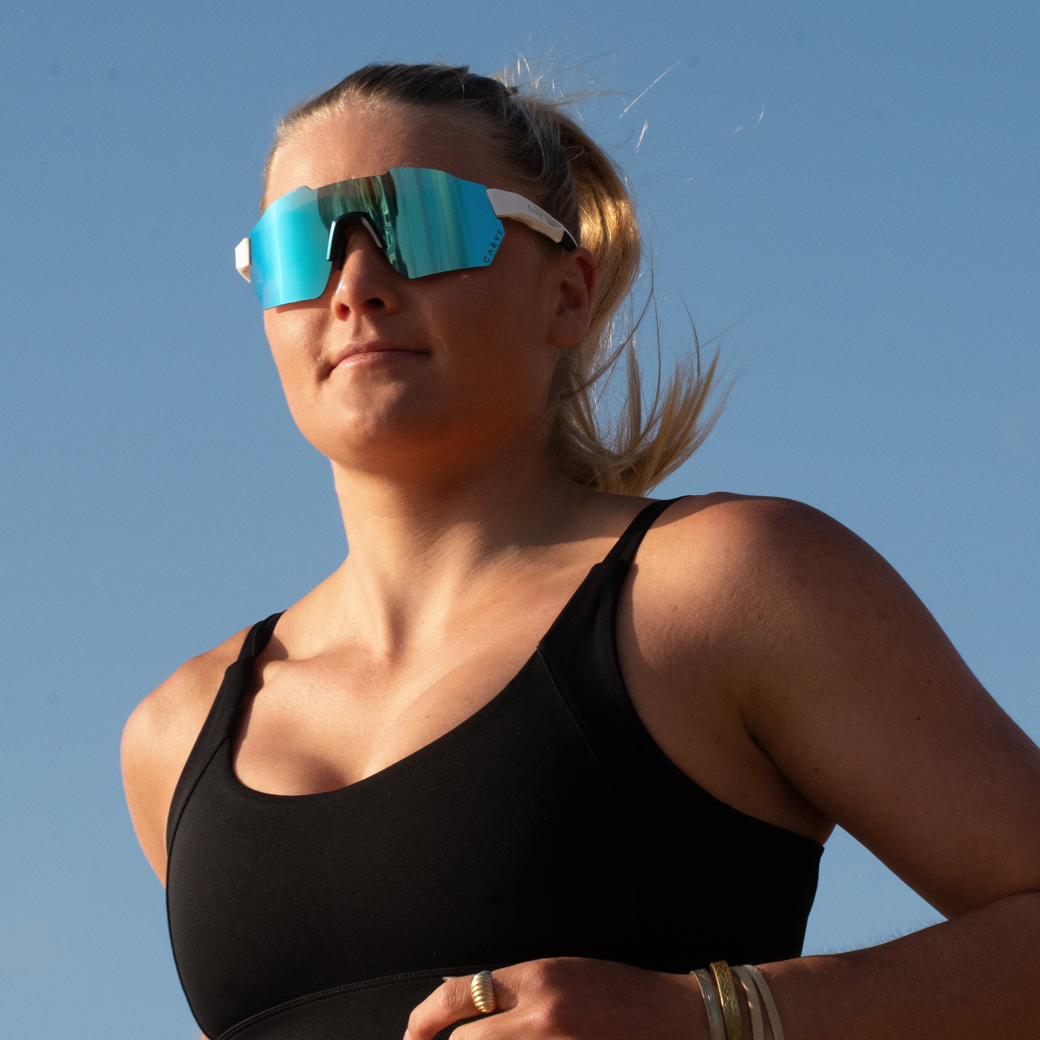 Woman wearing a black sports bra and sunglasses against a clear blue sky
