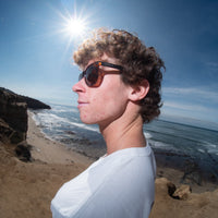 Person wearing sunglasses with a beach and ocean view through a circular lens.