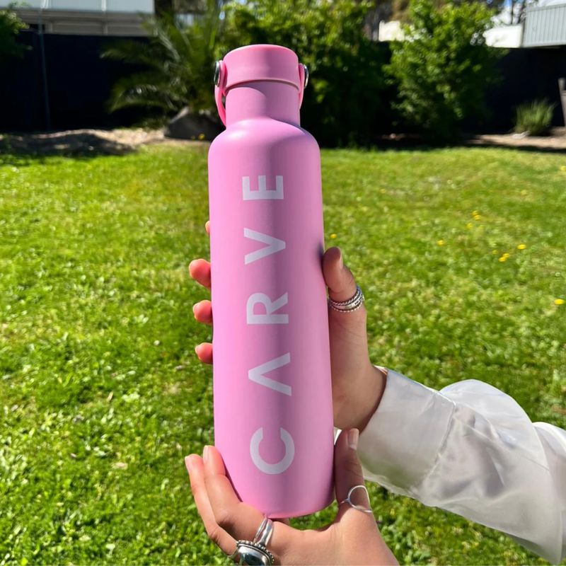 Pink water bottle with 'Carve' branding held in a hand outdoors.